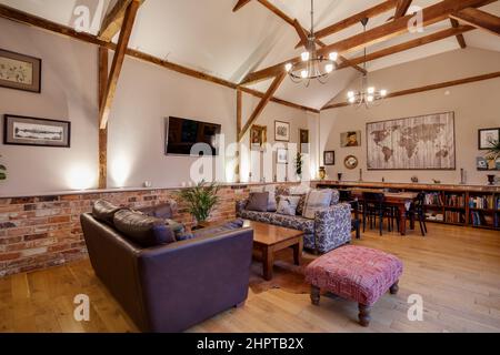 Traditionelles Wohnzimmer mit gewölbtem Gewölbe im umgebauten Scheunengebäude mit offenem Essbereich mit Sofas, Kaffee und Esstisch. Stockfoto