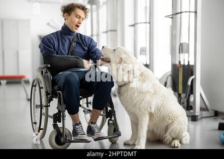 Typ mit Behinderungen im Rollstuhl mit seinem Assistenzhund im Rehabilitationszentrum Stockfoto