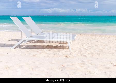 Zwei weiße Sonnenliegen befinden sich an einem sonnigen Tag an einem Sandstrand, Dominikanische Republik, Bavaro Beach Stockfoto