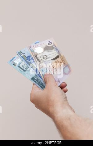 Eine Hand mit jordanischen Dinar-Banknoten über grauem Wandhintergrund, vertikales Foto mit selektivem Fokus Stockfoto