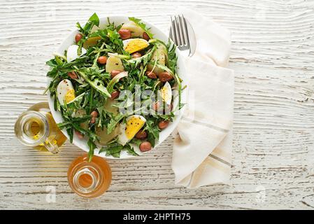 Frischer Dandelionssalat mit Bohnen, Kartoffeln und Eiern auf Holzboden Stockfoto