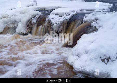 Eisfrei laufender Fluss im verschneiten Wald an einem düsteren kalten Wintertag Stockfoto