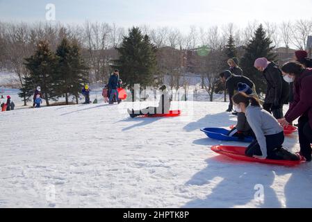 Toronto, Ontario / Canada - 02/21/2022: Familienaktivitäten unter COVID-19. Beim Rodeln im Winter tragen die Menschen eine schützende Gesichtsmaske. Stockfoto