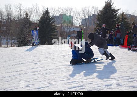 Toronto, Ontario / Canada - 02/21/2022: Familienaktivitäten unter COVID-19. Mutter und Kinder, die im Winter draußen Rodeln spielen. Stockfoto