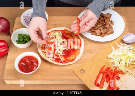 Die gehackten Paprika auf der Pita wie die nächste Dönerreihe anrichten. Hausgemachter Kebab. Stockfoto