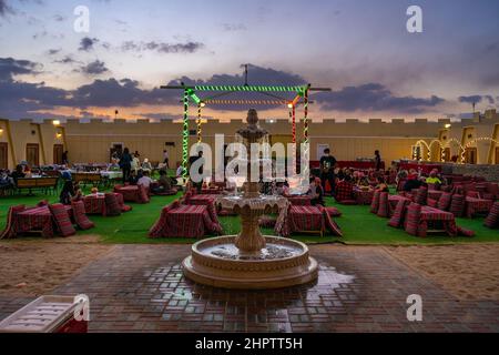 Dubai, VAE - 04 2021. Dezember: Menschen, die auf Kissen auf dem Boden sitzen und sich in einem traditionellen Desert Safari Camp unterhalten Stockfoto