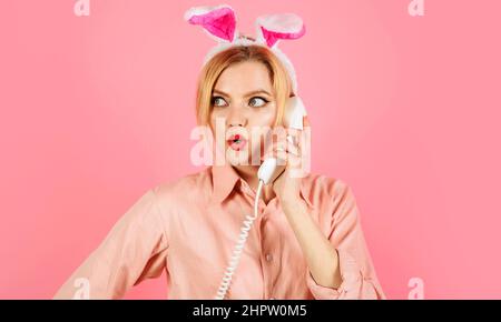 Kommunikation. Überraschte Frau in Hasenohren, die am Telefon sprach. Ostergrüße. Kaninchenmädchen. Stockfoto