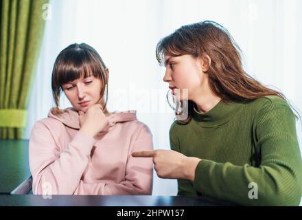 Junges wütendes Mädchen schimpft oder streitet ihre traurige verärgerte Freundin, winkt mit der Hand und stopft mit dem Finger. Missbrauch und Konfliktbeziehungskonzept. Stockfoto