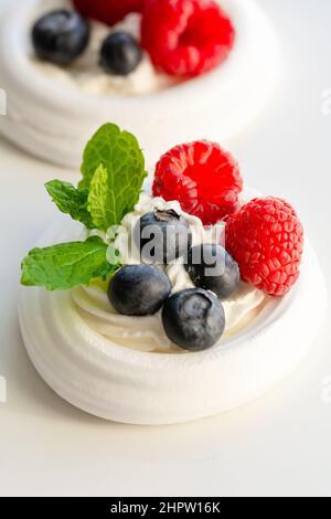 Meringue Nester mit Schlagsahne, Himbeeren, Blaubeeren und einem Minzblatt Stockfoto