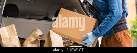 Postlieferer Kurier Mann trägt schützende Gesichtsmaske vor Von Transportwagen, der aufgrund des Coronavirus Pakethaltekasten liefert Krankheit oder COVID-19 Stockfoto