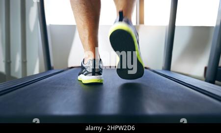 Der lange Weg zur Fitness. Kurzer Schuss eines nicht erkennbaren Mannes, der auf einem Laufband im Fitnessstudio joggt. Stockfoto