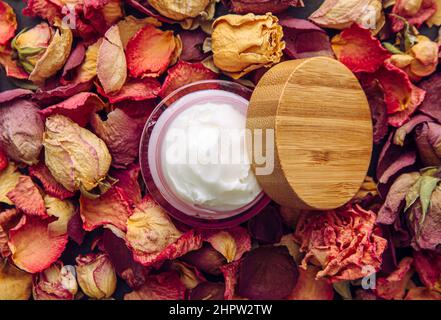 Rosa Farbglas mit samtiger Textur weißen handgefertigten Körper Butter Creme, trockene Rosenblätter und Puds Hintergrund, kopieren Raum. Stockfoto