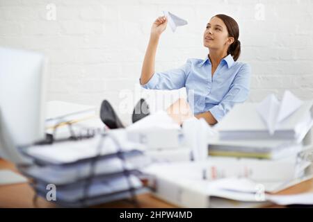 Die Papierkram ignorieren... indem Papierflugzeuge hergestellt werden. Aufnahme einer jungen Geschäftsfrau, die ein Papierflugzeug warf, während sie an ihrem Schreibtisch saß. Stockfoto