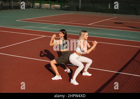 2 Mädchen trainieren gemeinsam im Freien. 2 Frau macht hockende Übungen Stockfoto