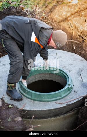 Ein Arbeiter installiert einen Kanalschachtler an einem Klärbecken aus Betonringen. Bau von Abwasserentsorgungsanlagen für Häuser. Stockfoto