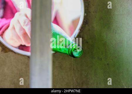 Frau oder weibliche Hand werfen leere grüne Glasflasche in Papierkorb Abfallbehälter. Natur Liebe, Abfallsortierung, Recycling, Pflege Konzept Idee. Stockfoto