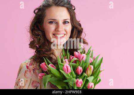 Porträt von lächelnden trendigen Frau mit langen welligen Brünette Haar mit Tulpen Bouquet auf rosa Hintergrund isoliert. Stockfoto