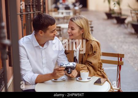 Lächelnde Frau, die am Tisch des Straßencafés mit einem hübschen Mann sitzt und Fotos überprüft Stockfoto