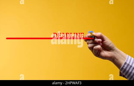 Rote Linie mit der Inschrift Deadline und eine weibliche Hand mit einem Marker auf gelbem Hintergrund. Das Konzept der Festlegung von Fristen Stockfoto