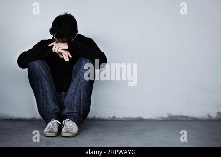 Hes hat eine harte Zeit. Ein junger Mann, der traurig aussieht, während er mit dem Kopf auf den Händen auf dem Boden sitzt. Stockfoto