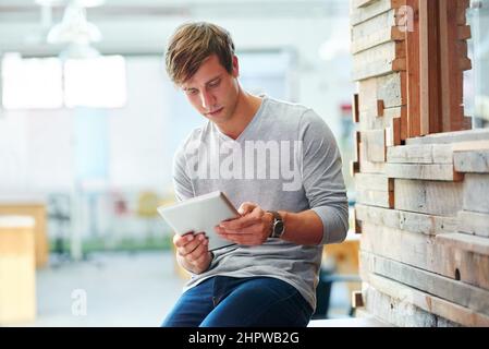 Eine Pause mit seinem Tablet machen. Aufnahme eines Designers, der ein digitales Tablet verwendet, während er im Büro arbeitet. Stockfoto