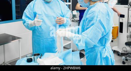 Chirurgen helfen sich gegenseitig, sterile Operationshandschuhe anzuziehen. Selektiver Fokus. Stockfoto