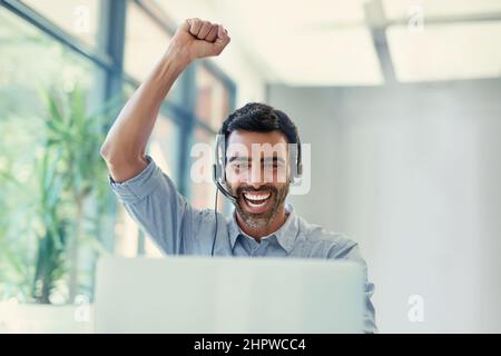 HES hat gerade einen weiteren Deal eingesackt. Eine kurze Aufnahme eines Callcenter-Agenten, der eine Faustpumpe macht, während er in einem Büro an einem Laptop arbeitet. Stockfoto