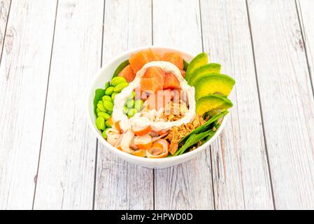 Gewürfelte Lachsschüssel mit Avocado-Scheiben, Edamame-Bohnen, Surimi-Scheiben, knuspriger Zwiebel und Spinat Stockfoto