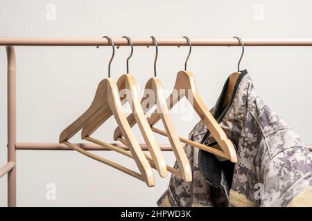 Kleiderbügel aus Holz hingen an einer hellbraunen Bar oder Kachel, einige waren leer und die andere mit einem städtischen Tarnstoff-Kleidungsstück Stockfoto