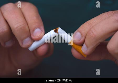 Hören Sie auf zu rauchen, hören Sie auf zu rauchen oder rauchen Sie keine Zigaretten. Mann, der eine zerbrochene Zigarette in den Händen hält. Mann, der Zigaretten ablehnt. Beende schlechte Angewohnheit. Stockfoto