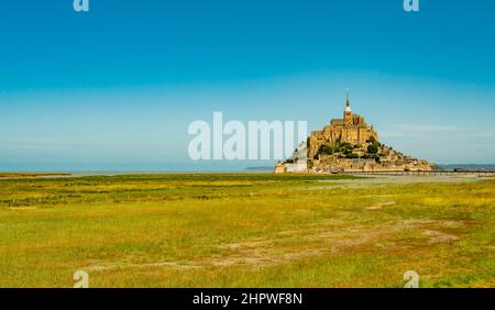 Atemberaubende Aussicht auf die berühmte Gezeiteninsel Le Mont Saint Michel an einem hellen sonnigen Tag mit leeren grünen Feldern, Normandie, Nordfrankreich Stockfoto