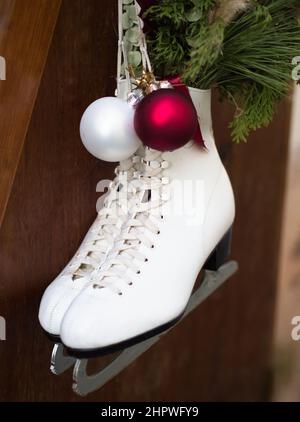 Weiße Schlittschuhe, die am Holzzaun mit Weihnachtsdekoration hängen Stockfoto