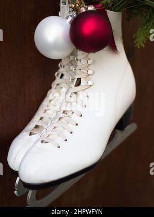 Weiße Schlittschuhe, die am Holzzaun mit Weihnachtsdekoration hängen Stockfoto