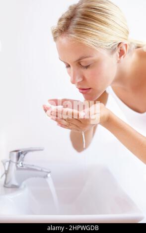 Erhaltung einer gesunden und schönen Haut. Aufnahme einer attraktiven jungen Frau, die ihr Gesicht über einem Waschbecken mit Wasser wäscht. Stockfoto