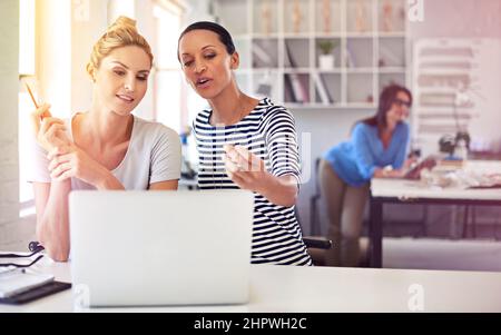 Ihre Entwürfe im Detail zu diskutieren. Aufnahme von zwei Kollegen, die in einer Boutique zusammen einen Laptop benutzen. Stockfoto