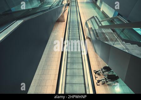 Ein Blick von oben auf einen Flughafen oder einen Bahnhof oder ein modernes Shopping: Ein langer Fahrtravelator, eine bewegliche Treppe auf der linken Seite und die Treppe Stockfoto