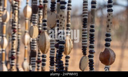 Nahaufnahme von Schnüren afrikanischer Halsketten aus Perlen und Samen, die auf einem Outdoor-Markt in Namibia ausgestellt werden. Hintergrund unscharf oder unscharf Stockfoto