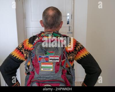 Mann im Rollstuhl, der sich auf die Reise vorbereitet. Er verlässt das Haus, mit dem Rücken zum Betrachter. Hes einen Rucksack auf seinem Rücken, der mit bedeckt ist Stockfoto