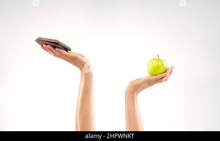 Warum kann ich mich nicht für beides entscheiden? Studioaufnahme einer unkenntlichen Frau, die sich vor grauem Hintergrund zwischen gesunden und ungesunden Lebensmitteln entscheidet. Stockfoto