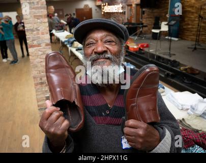 Marietta, Georgia, USA. 13th. Februar 2022. Ein Obdachloser zeigt seine Freude, ein Paar Schuhe von Tischen mit gespendeter Kleidung in der First Baptist Church in Marietta, Georgien, zu finden, während eines Abendessens für Einzelpersonen oder Familien, die finanziell oder obdachlos sind. (Bild: © Robin Rayne/ZUMA Press Wire) Stockfoto