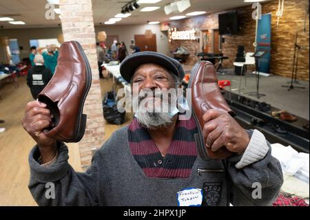 Marietta, Georgia, USA. 13th. Februar 2022. Ein Obdachloser zeigt seine Freude, ein Paar Schuhe von Tischen mit gespendeter Kleidung in der First Baptist Church in Marietta, Georgien, zu finden, während eines Abendessens für Einzelpersonen oder Familien, die finanziell oder obdachlos sind. (Bild: © Robin Rayne/ZUMA Press Wire) Stockfoto