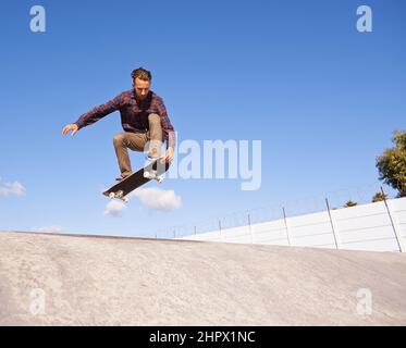 Perfektioniert seine Tricks. Ein junger Mann macht Tricks auf seinem Skateboard im Skatepark. Stockfoto