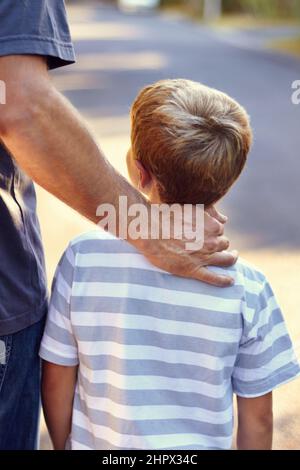 Die führende Hand eines fürsorglichen Vaters. Rückansicht eines Vaters und eines Sohnes, der zusammen die Straße entlang geht. Stockfoto