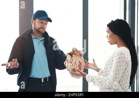 Es tut mir leid, aber ich kann nichts dagegen tun. Aufnahme eines hübschen Lieferers, der in der Lobby mit einer unzufriedenen Kundin verhandelt. Stockfoto