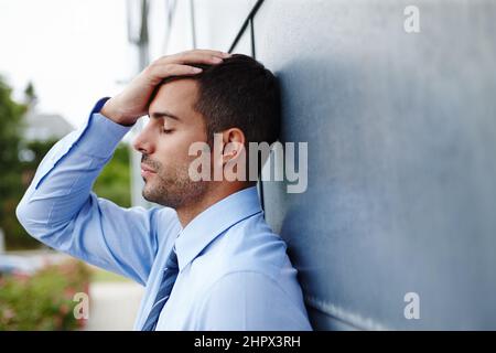 Gefeuert Ein gestresster junger Geschäftsmann, der draußen mit dem Kopf in den Händen steht. Stockfoto