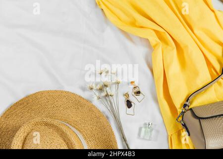 Strohhut, gelbes Kleid, Strohsack auf weißem Hintergrund. Trendiges Sommeroutfit. Flat Lay mit Kleidung für Urlaub und Urlaub. Stockfoto