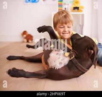 Jeder kleine Junge sollte seinen eigenen Hund haben. Ein kleiner Junge, der mit seinem Hund in seinem Zimmer spielt. Stockfoto