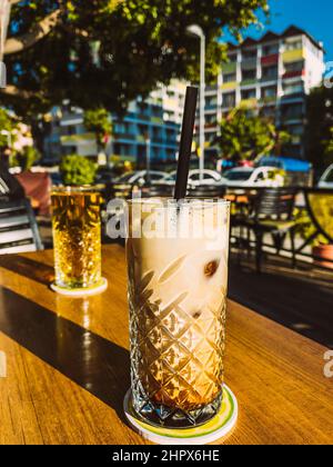 Glastasse mit kaltem Kaffeegetränk auf dem Tisch im Straßencafé. Stockfoto