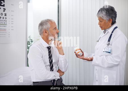 Drei Tabletten, zweimal am Tag. Eine reife Ärztin, die einer ihrer Patienten während einer Untersuchung eine Flasche Pillen gab. Stockfoto