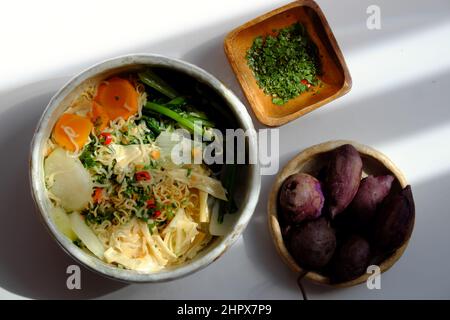 Vietnamesische vegane Mahlzeit zum schnellen Frühstück, Instant-Nudel-Koch mit Senfblatt, Karotte, Rübe, Tofu-Haut, Schüssel mit Nudelsuppe auf weißem Hintergrund Stockfoto